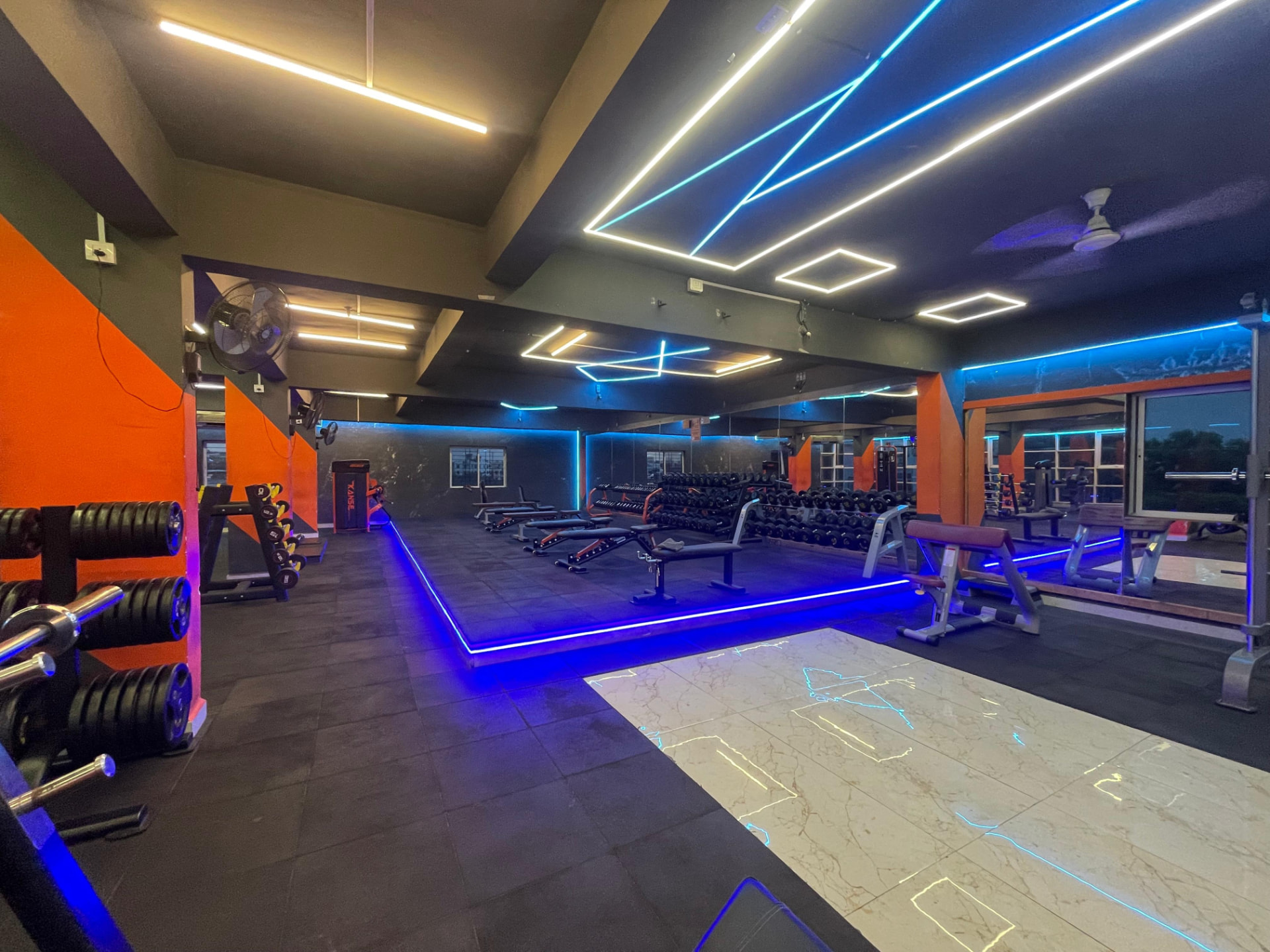 Free weights hall with adjustable benches, dumbbell racks and blue LED floor lighting at SK Fitness Gym Kharadi